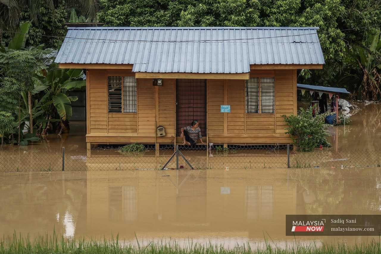 Gambar fail seorang wanita duduk di hadapan pintu rumahnya ketika banjir.