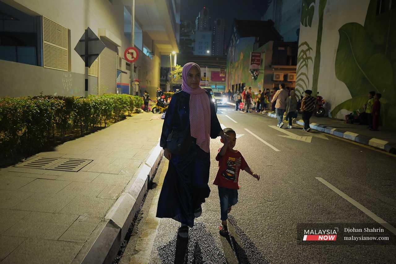 Ana memimpin tangan anaknya ketika beratur untuk mendapatkan sumbangan yang diagihkan di Jalan Chow Kit.