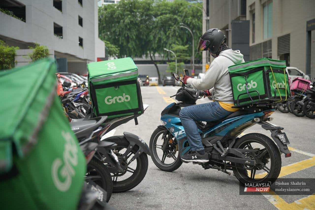 Seorang penghantar makanan Grab menerima tempahan melalui telefon bimbitnya di kawasan beli-belah di Bukit Bintang di Kuala Lumpur.