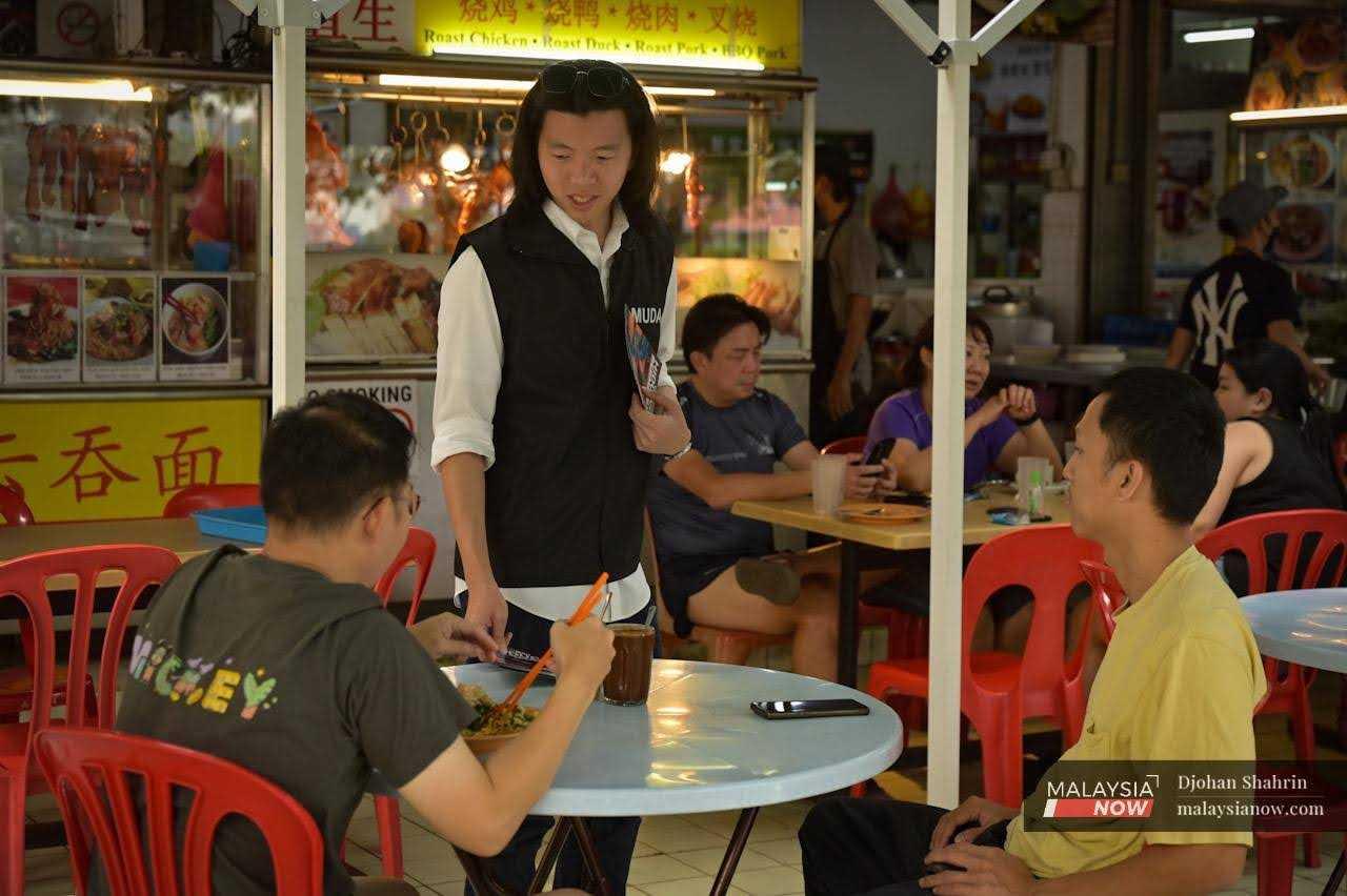 Muda's candidate for Seri Setia, Dobby Chew, distributes flyers to customers at a coffee shop in Kelana Jaya as part of his campaign for the Selangor election. 
