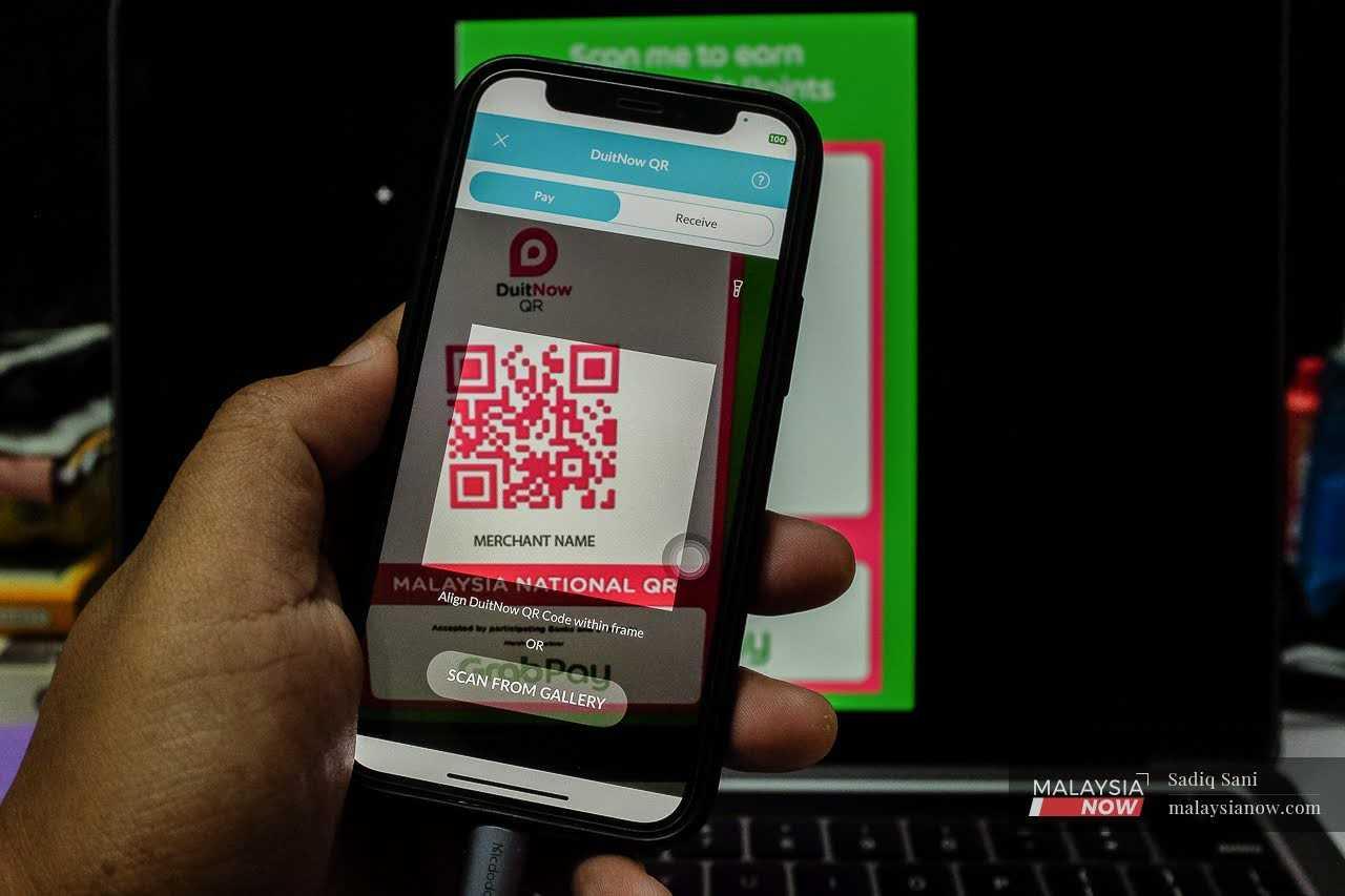 A customer scans a DuitNow QR code to make an online payment at a shop.
