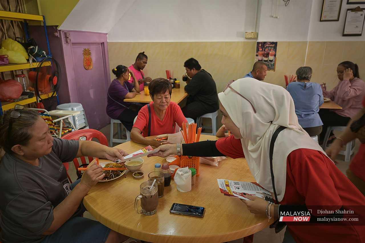 Calon Parti Rakyat Malaysia Hafizah Zainuddin mengedarkan risalah berkaitan manifesto dan maklumat dirinya kepada pelanggan di sebuah kedai kopitiam di pekan Kuala Kubu Baharu.