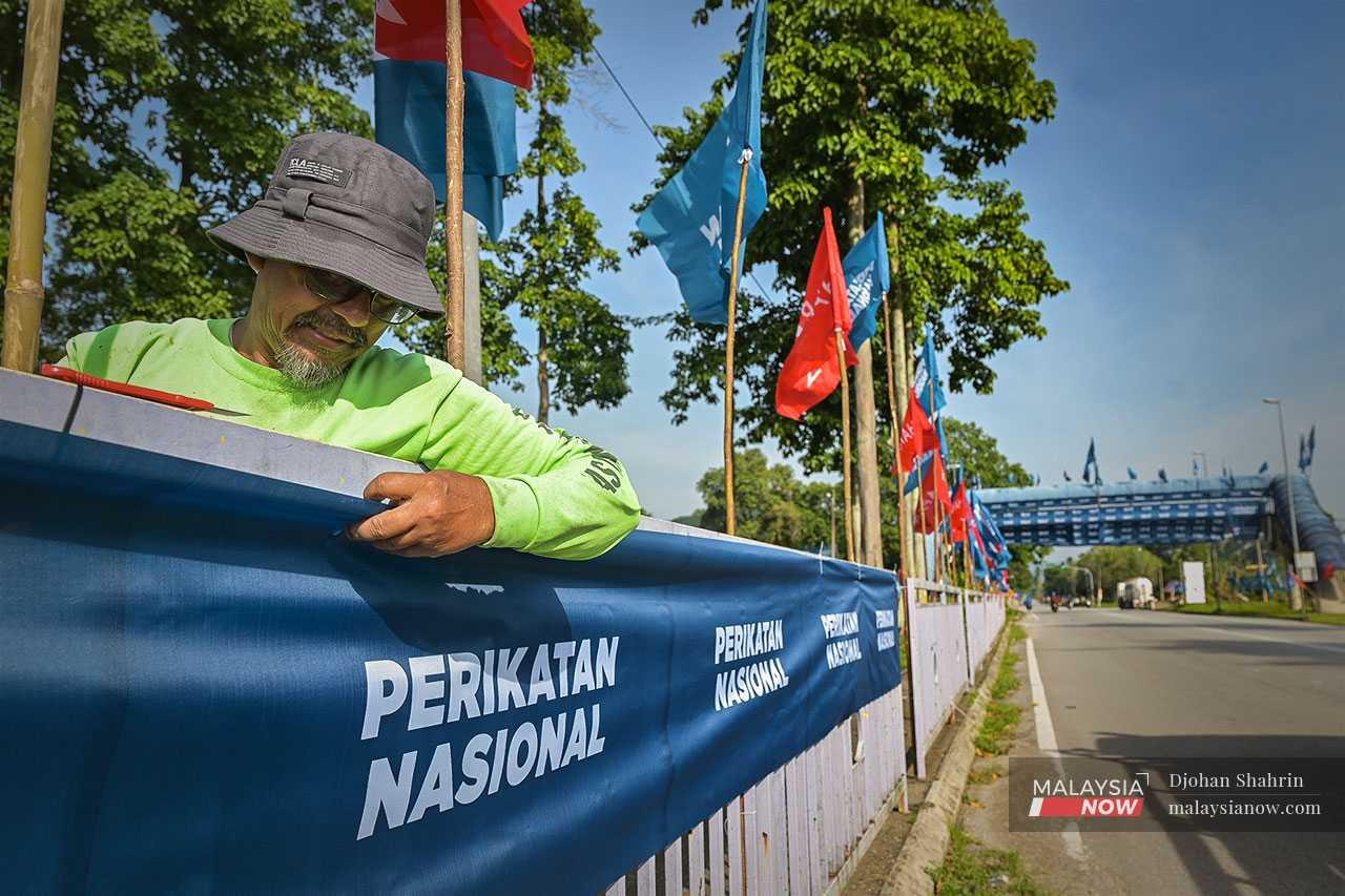 A party worker fastens a Perikatan Nasional banner along a road in Batang Kali.