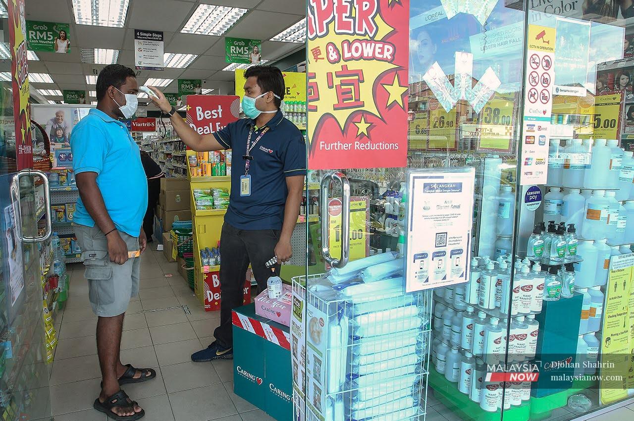 A customer has his temperature checked with a handheld thermometer before entering a pharmacy.