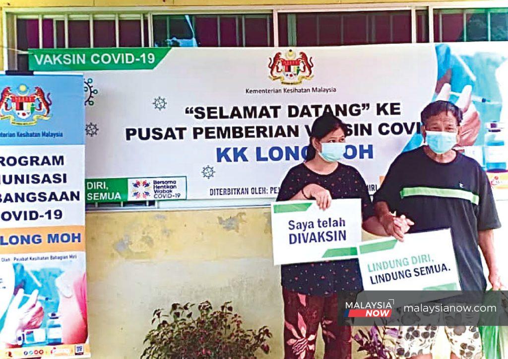 Ukeng Lian dan anak perempuannya yang merupakan anak berkeperluan khas memegang plakad 'Saya telah divaksin' di Klinik Kesihatan Long Moh.