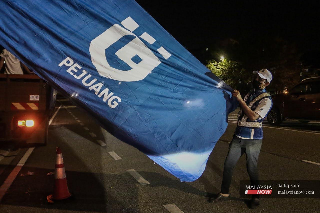 A volunteer unfurls a Pejuang flag to be set up near a road in Larkin, Johor Bahru, ahead of the state election on March 12.
