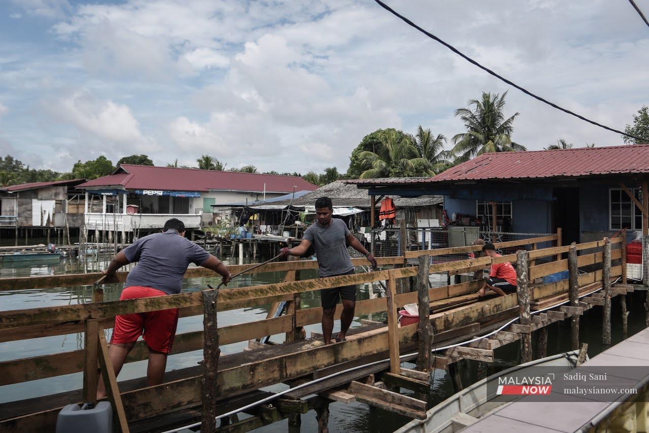 Orang Asli men from the Seletar tribe work together to repair a wooden bridge outside their homes in Kampung Sungai Temun in Johor Bahru.