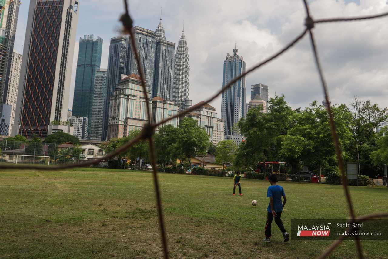 Kanak-kanak bermain bola sepak di sebuah padang kecil dilatari pemandangan Menara Berkembar Petronas.