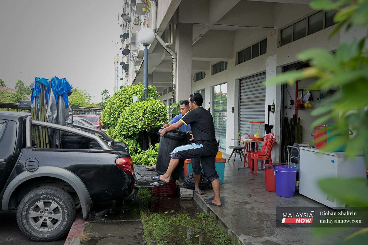 One of his workers helps him hoist a plastic barrel full of juice into the back of a pickup truck, to be taken to his roadside stall. 