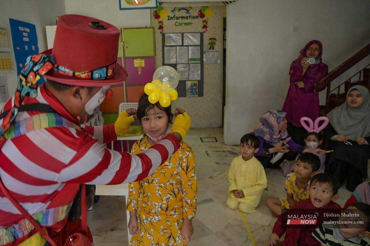 Awang the Clown fastens a yellow balloon flower to the head of a little girl to match her dress. 