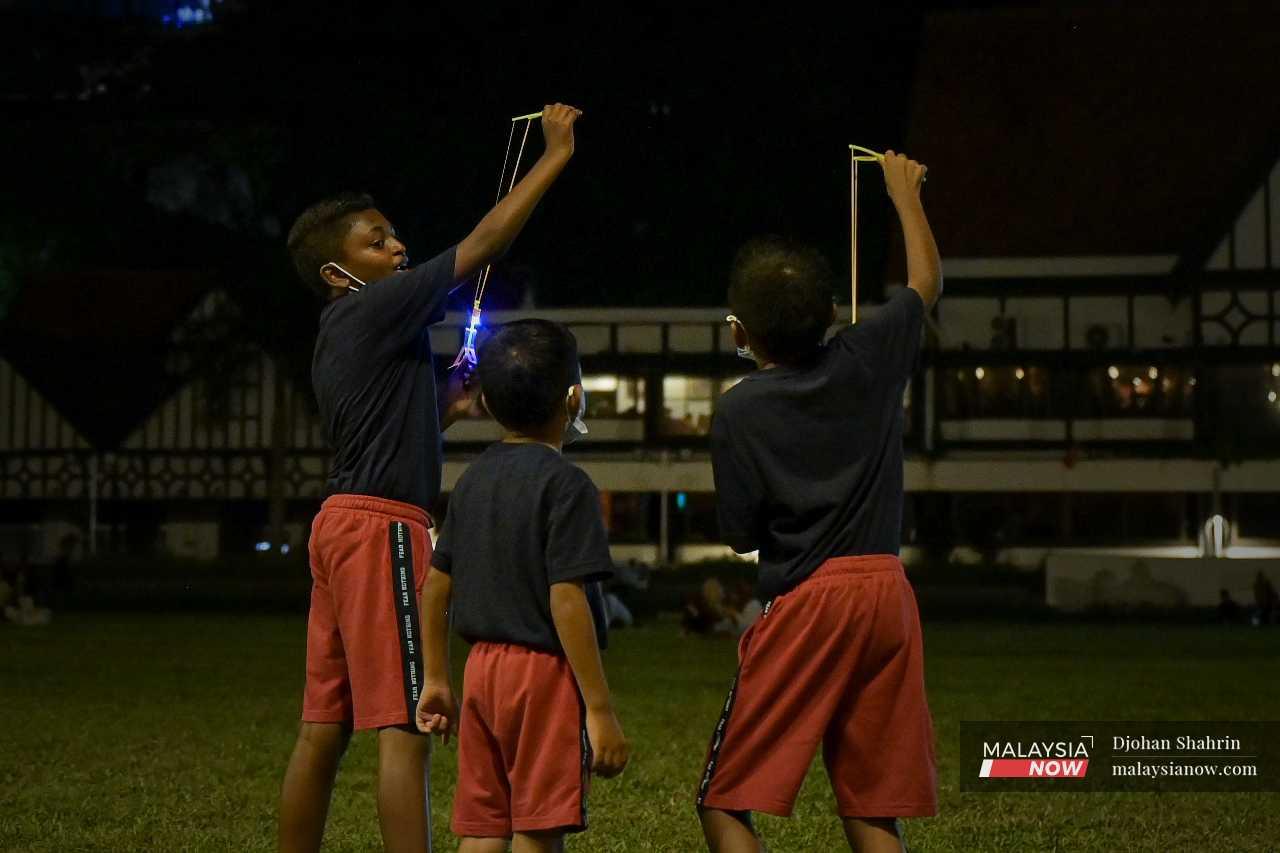 Sekumpulan kanak-kanak bermain lastik berlampu di padang Dataran Merdeka.