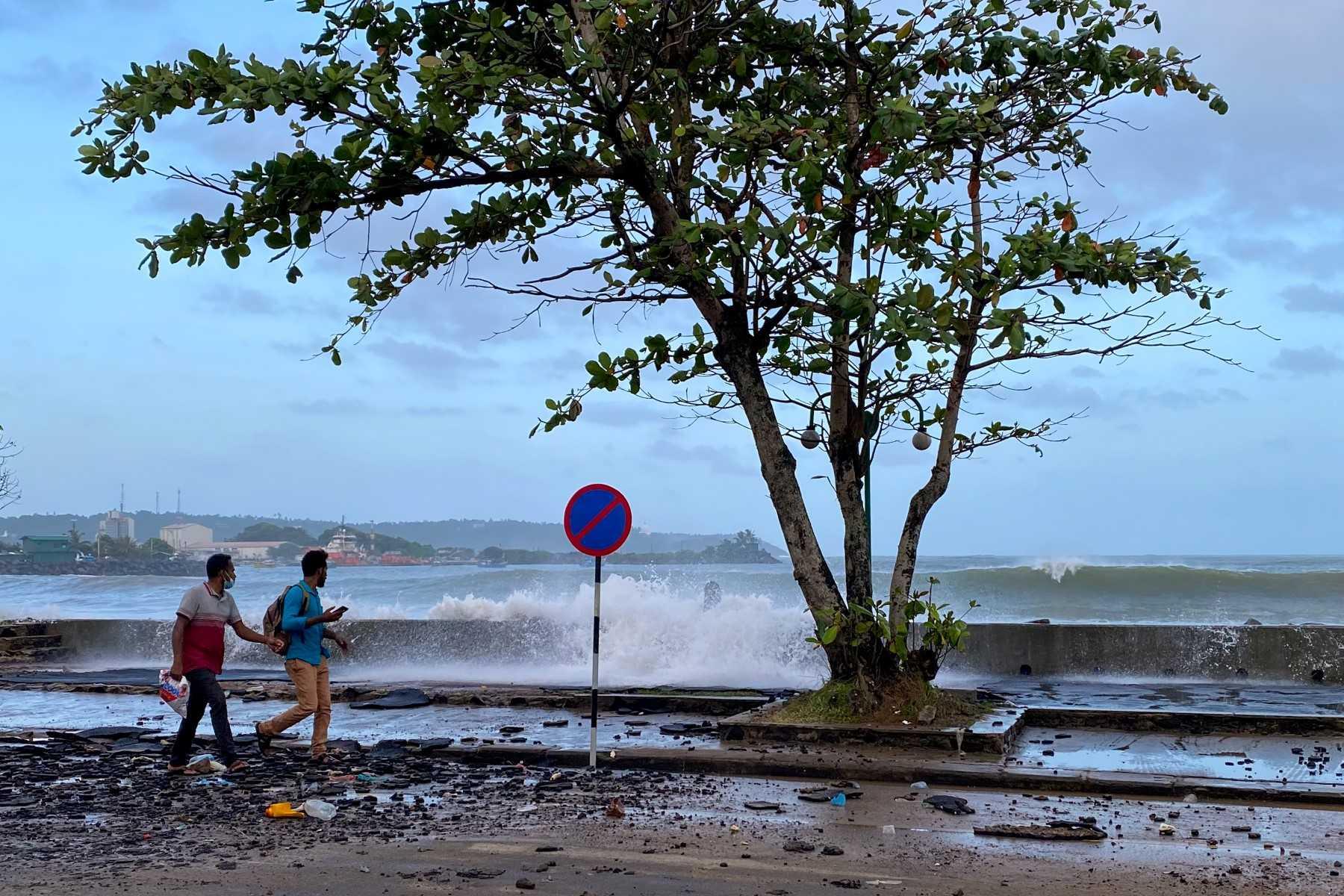 People walk along a road as waves crash over the promenade during monsoon winds in Galle on July 2. Photo: AFP