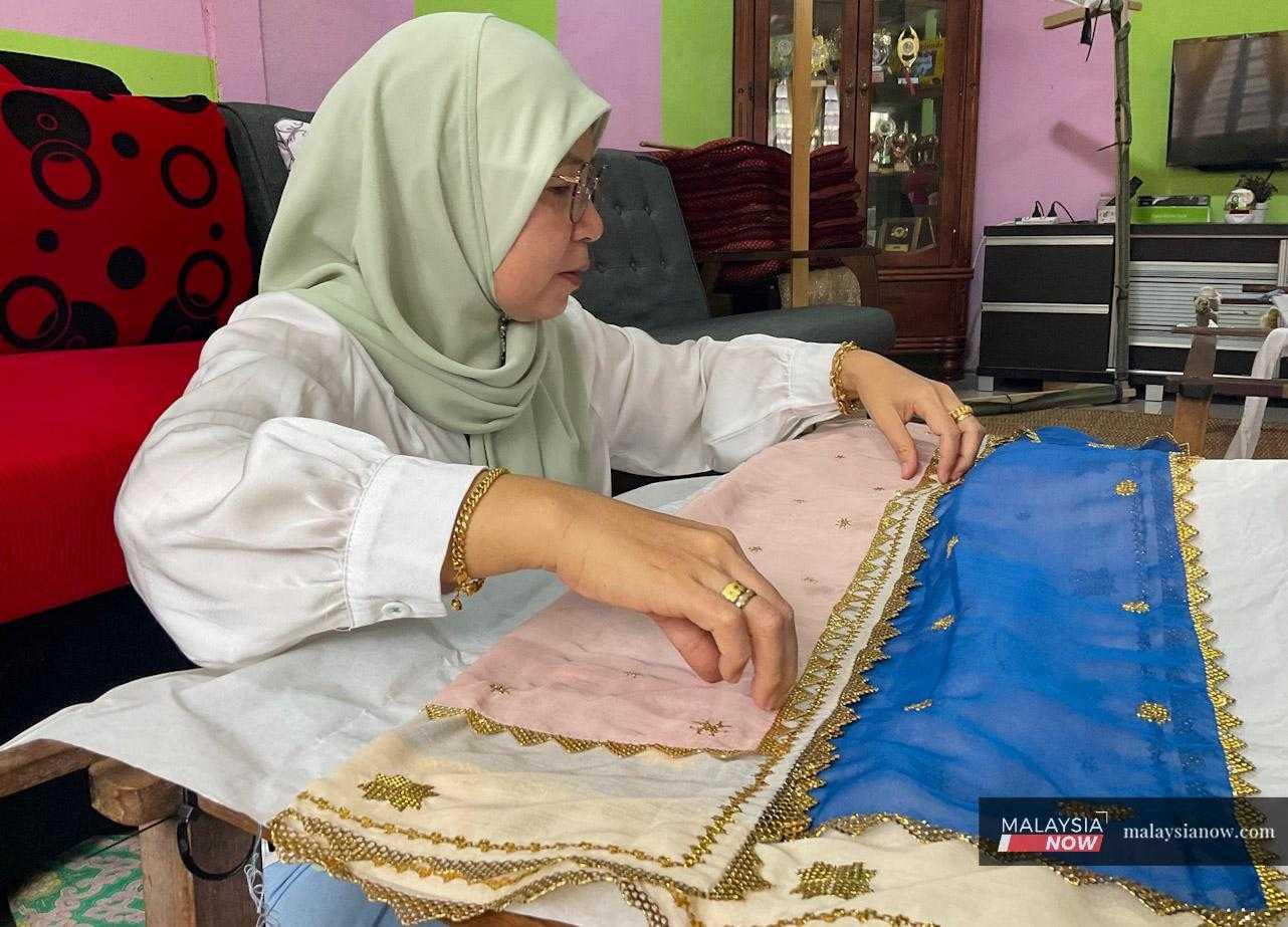 Ros Salleh, a keringkam weaver from Kampung Darul Islam Belimbing in Puncak Borneo, folds a stack of embroidered headscarves.  
