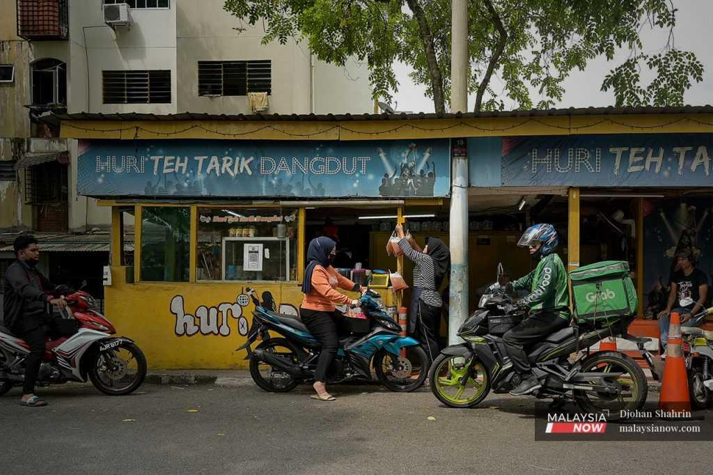 Pelanggan yang menunggang motorsikal berhenti di hadapan Huri Teh Tarik Dangdut di Taman Medan, Petaling Jaya, di mana Huri menjual minuman sejuk dengan harga murah sejak 20 tahun lalu.