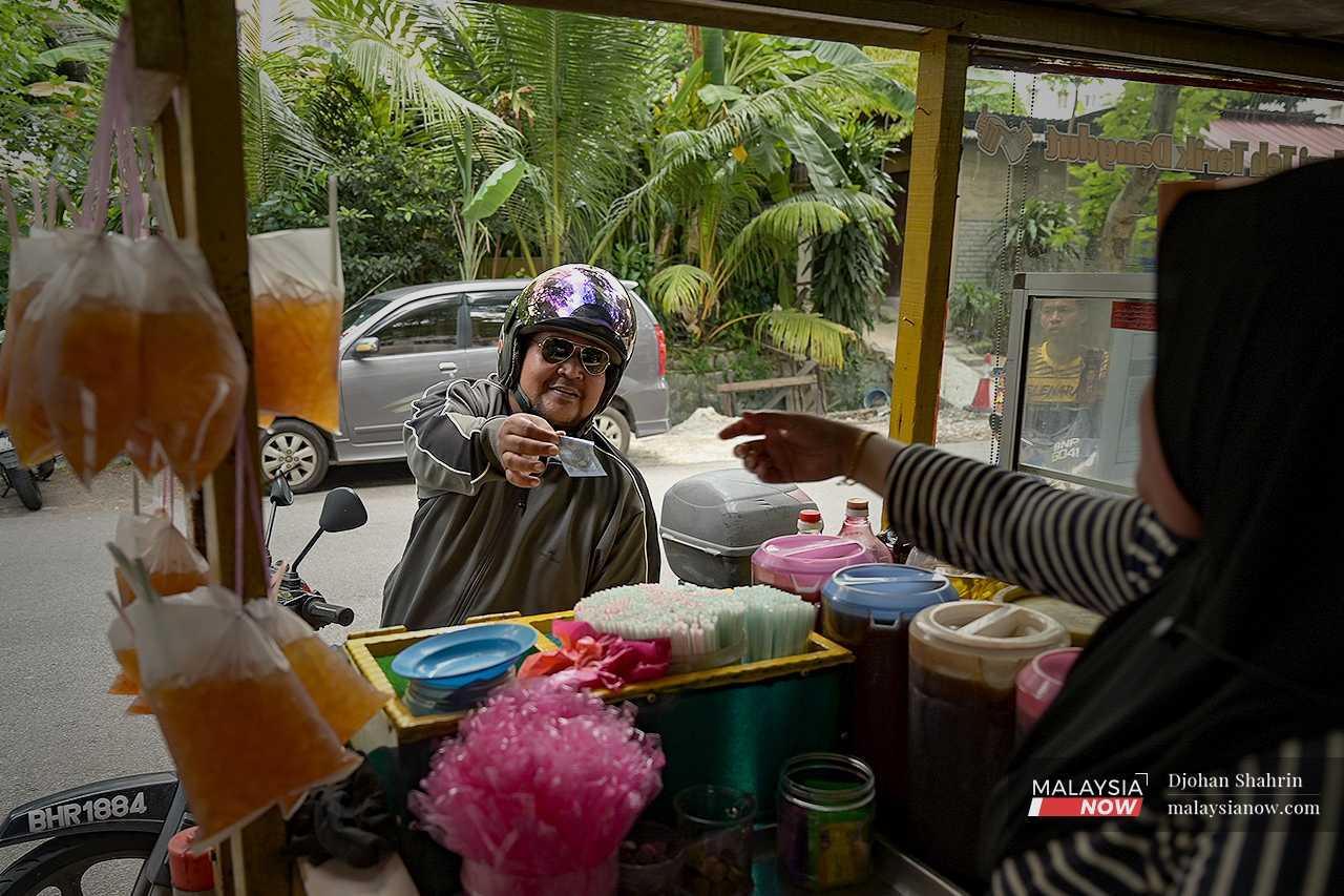 Seorang pelanggan tersenyum sambil membayar RM1 untuk sebungkus teh o ais.