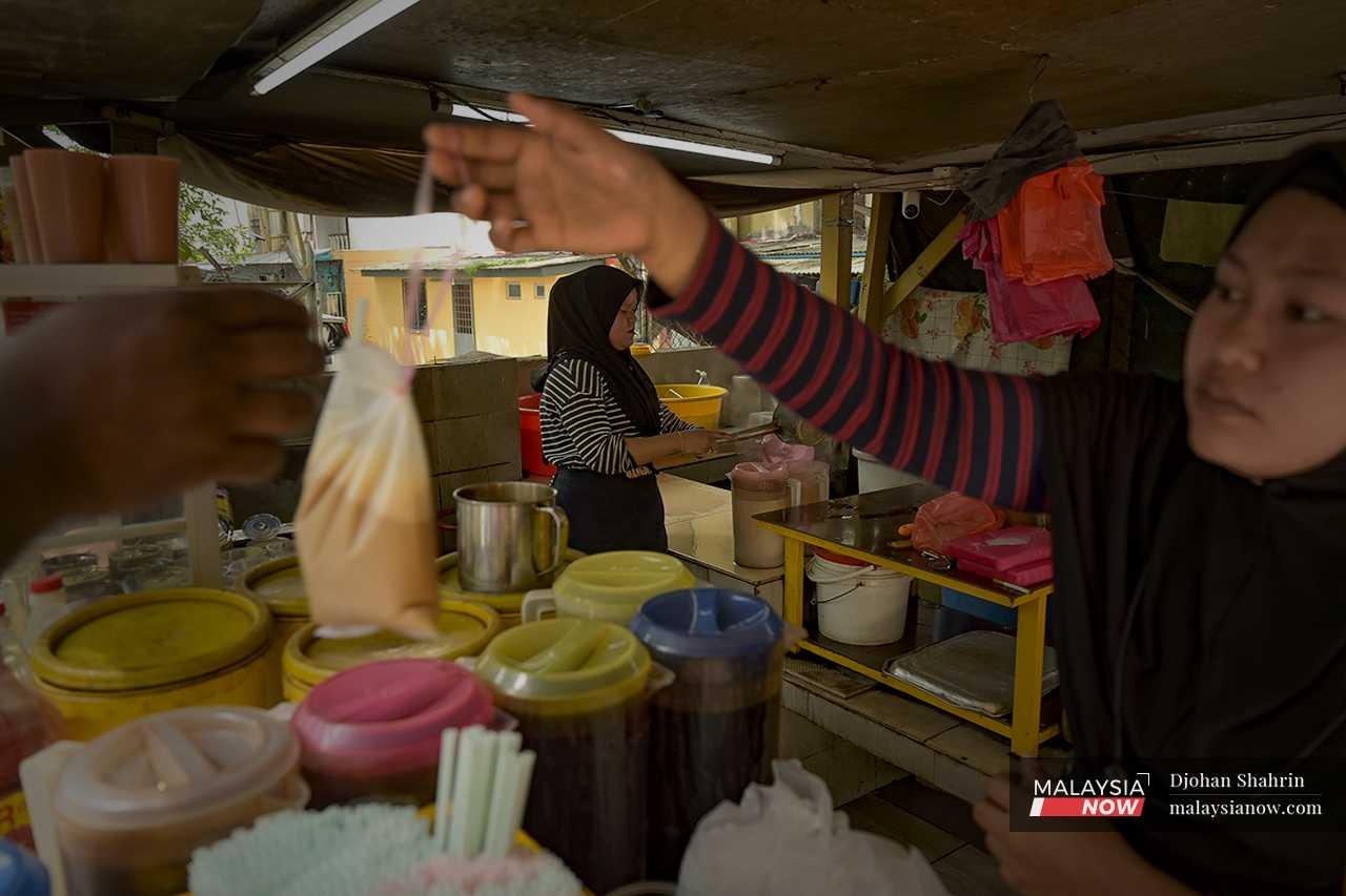 Seorang pekerja menyerahkan sebungkus teh tarik, yang dibancuh bersama susu manis.