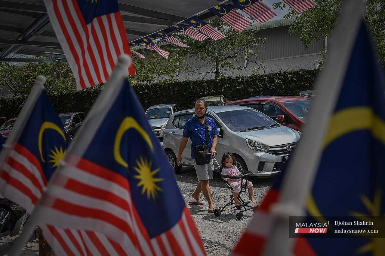 Seorang bapa berjalan sambil menolak kereta sorong bayi di ibu negara ketika melalui deretan Jalur Gemilang.