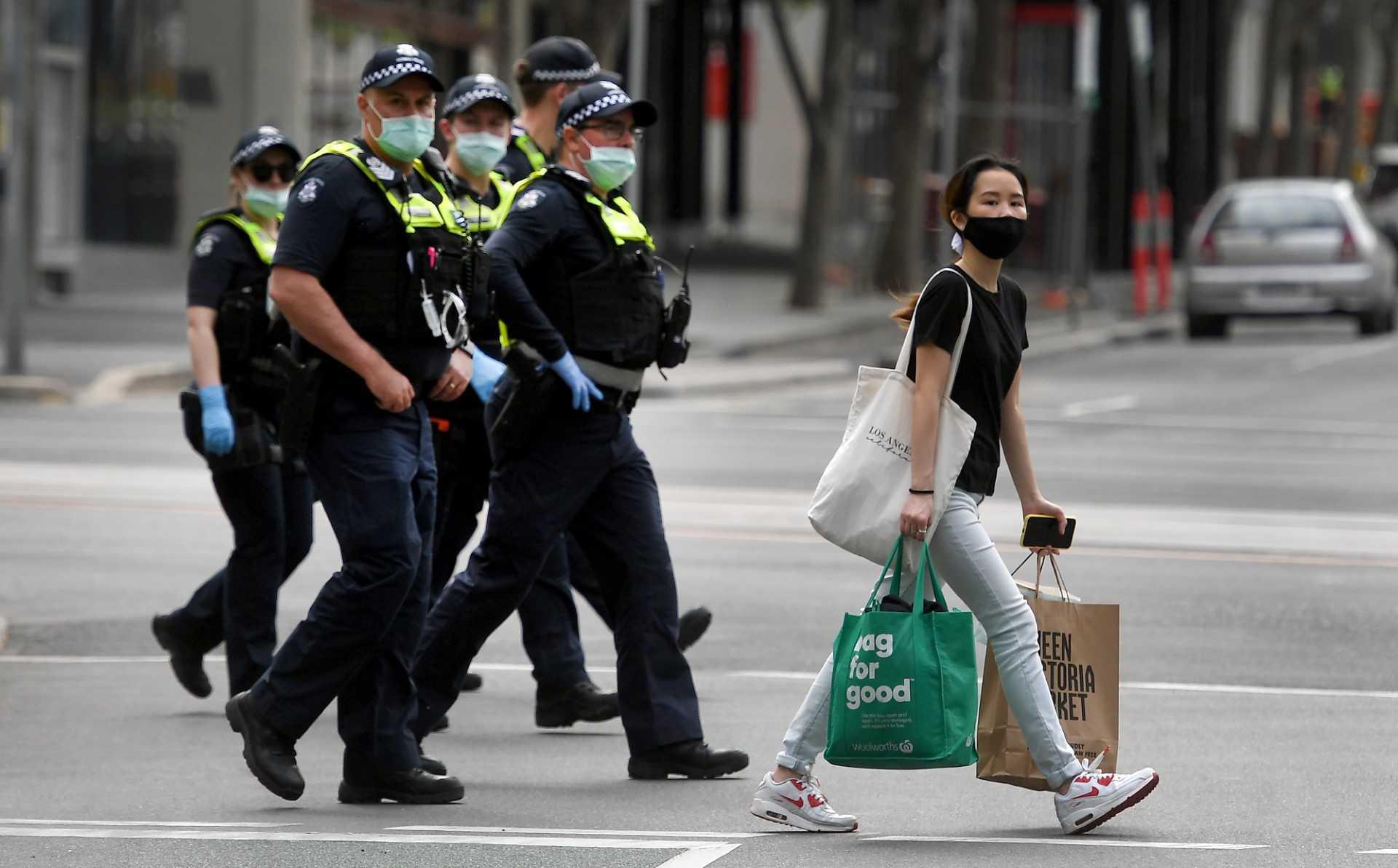 A woman crosses the road with her shopping while police officers patrol through the streets of Melbourne on Sept 29, 2021. Photo: AFP