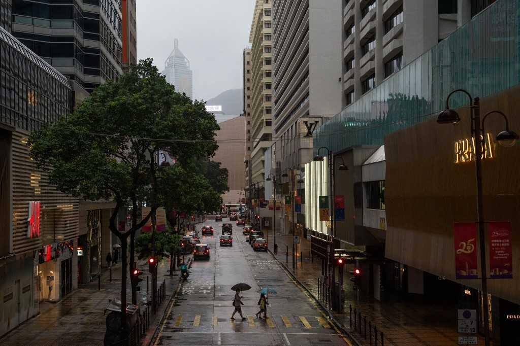 People shelter from the rain with umbrellas while crossing a street in Hong Kong on July 2. In a bid to appease protesters and contain the crisis, regulators and local governments have stepped up efforts to reassure critics that projects will be completed. Photo: AFP
