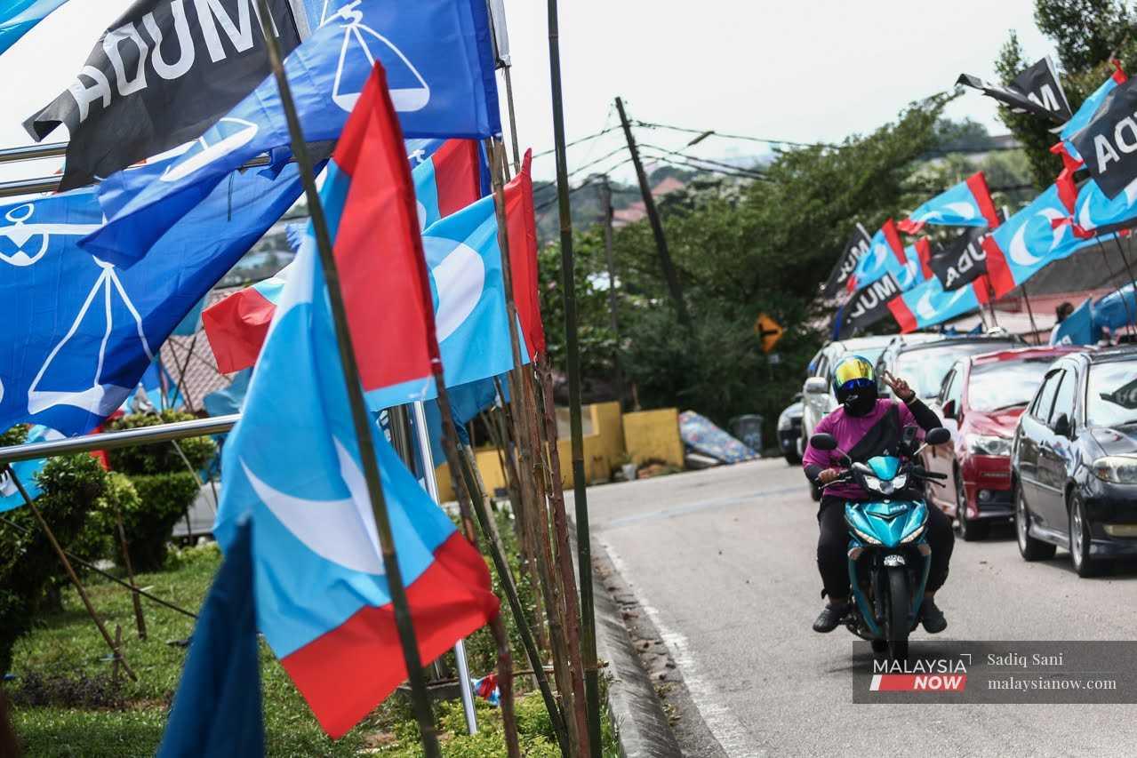 A motorcyclist holds up a peace sign as he passes a junction decorated with party flags, including that of PKR, near Kampung Melayu Majidee, ahead of the Johor state election on March 12.