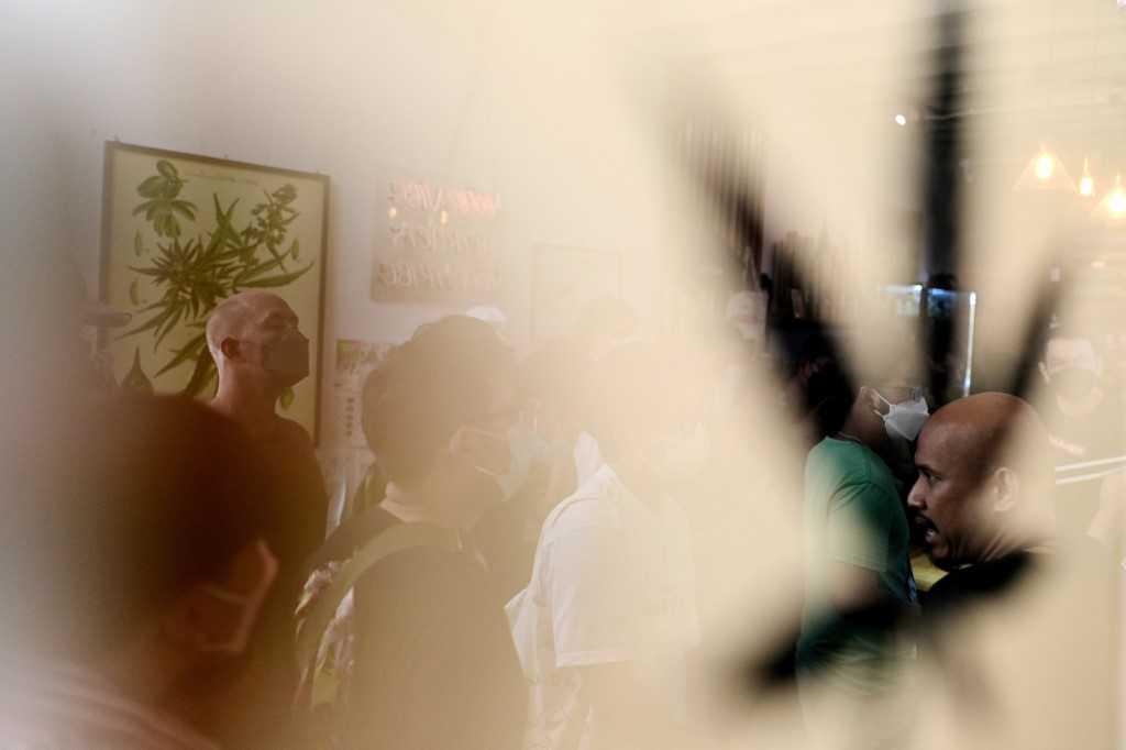 People are reflected in a glass frame as they queue to buy cannabis at the Highlands cafe in Bangkok on June 9. Photo: AFP