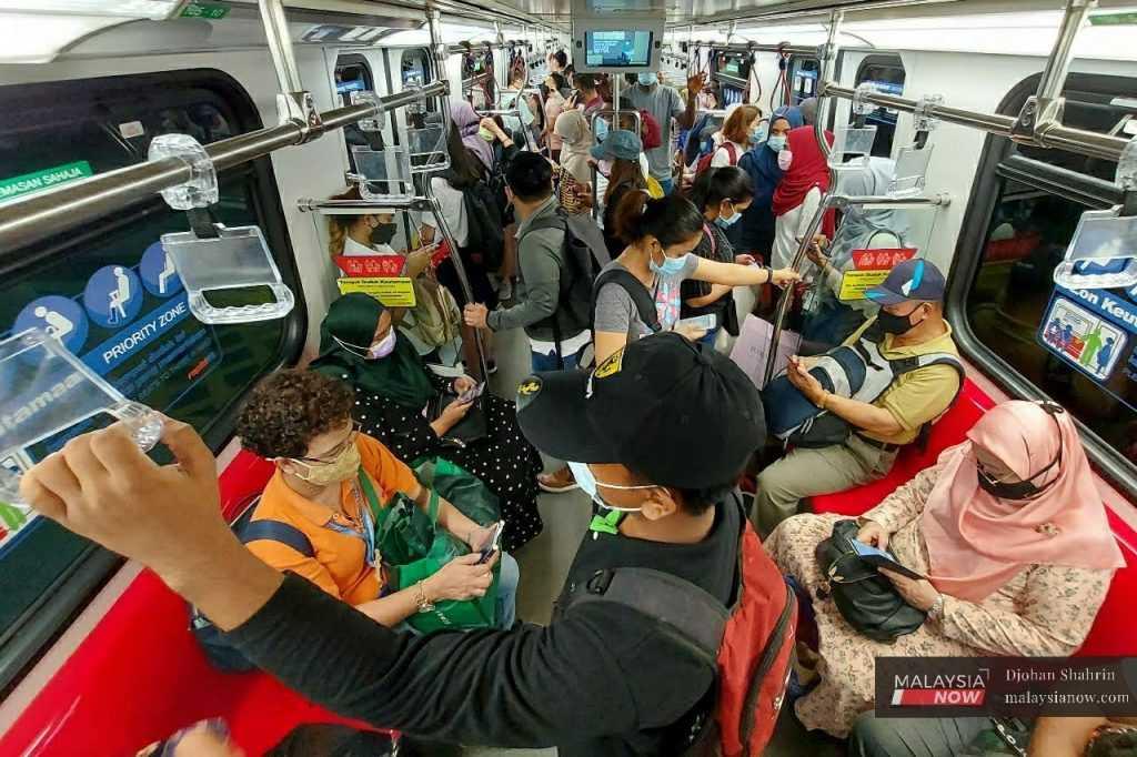 Penumpang LRT memakai pelitup muka bagi mengelak jangkitan Covid-19 menatal telefon pintar mereka di Kuala Lumpur. 