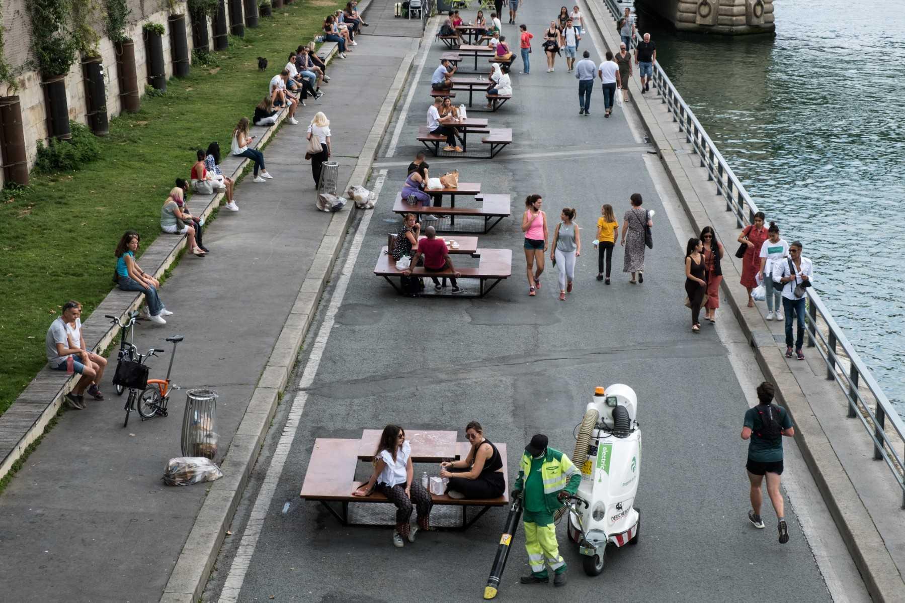 A street cleaner cleans the sidewalk as pedestrians walk and sit on tables along the Seine river in Paris on Sept 4. Photo: AFP