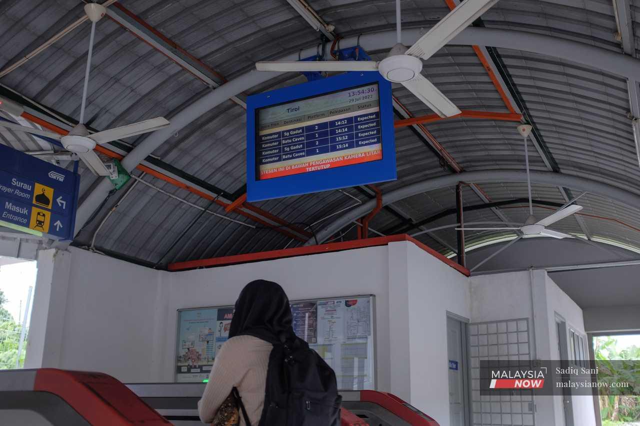 A passenger passes beneath a time table showing the KTM schedule at the Tiroi station.