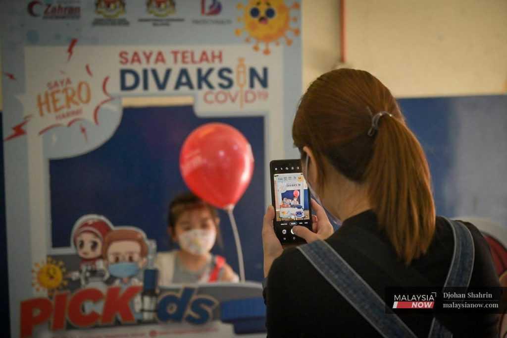 A woman takes a picture of her daughter at the photo booth set up at the Dewan Komuniti Taman Bukit Mewah vaccination centre in Kajang.