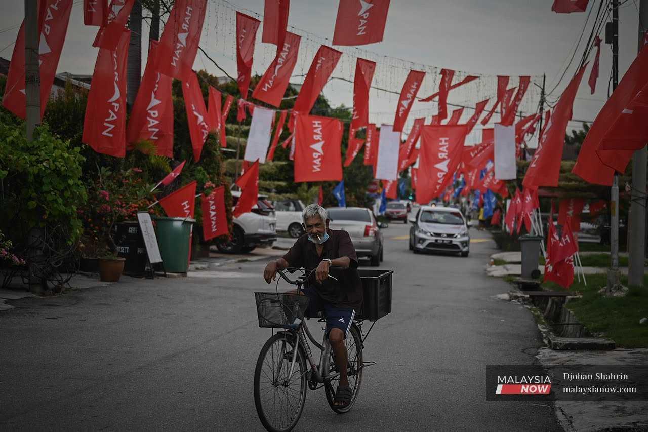 Seorang warga emas mengayuh basikan di bawah gantungan bendera Pakatan Harapan di Melaka menjelang pilihan raya negeri itu tahun lalu. 