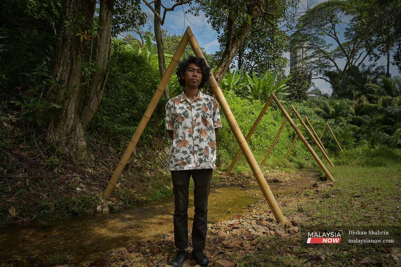 Artist Poodien poses for a photo with his artwork, 'Here is Certain', constructed from bamboo over another small stream. 