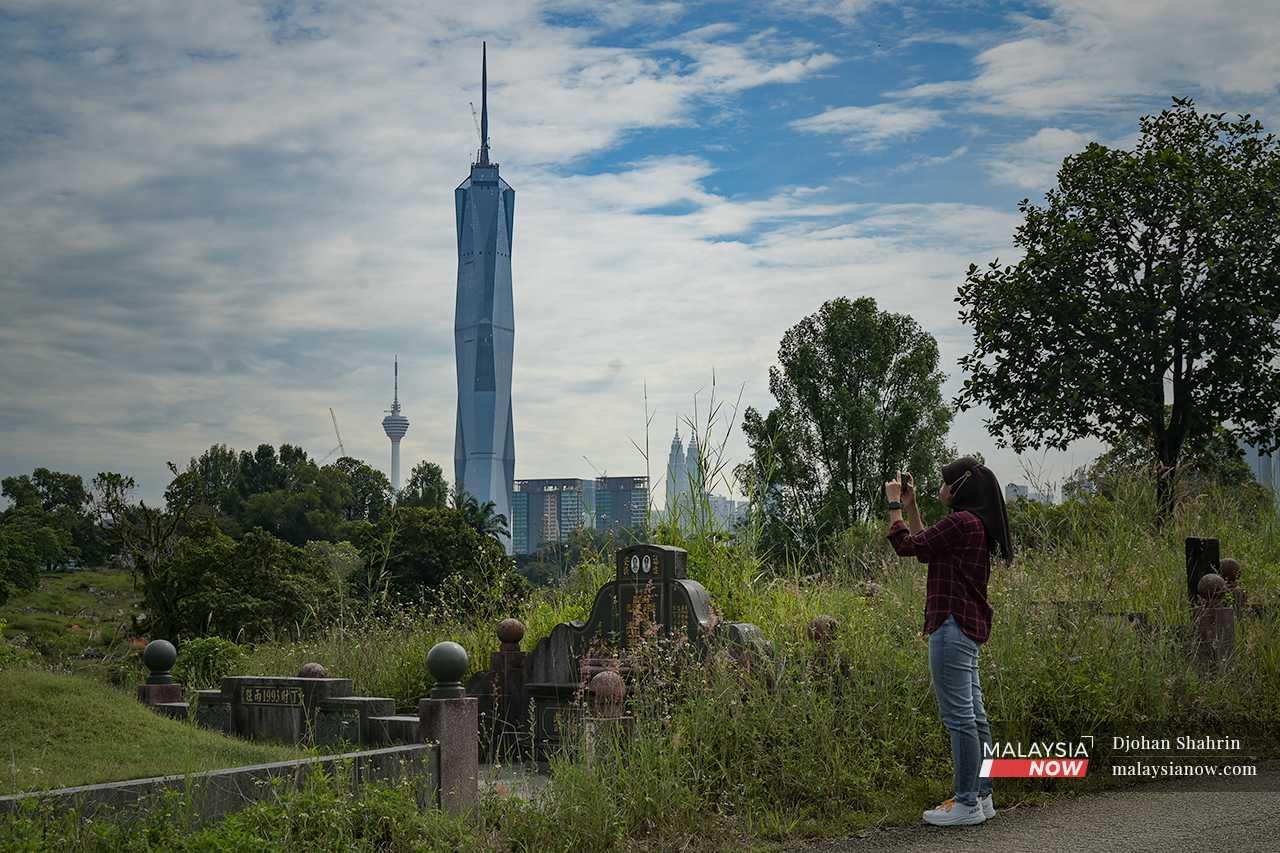 A visitor takes a picture of the Kuala Lumpur landscape from a hill on the cemetery grounds. 