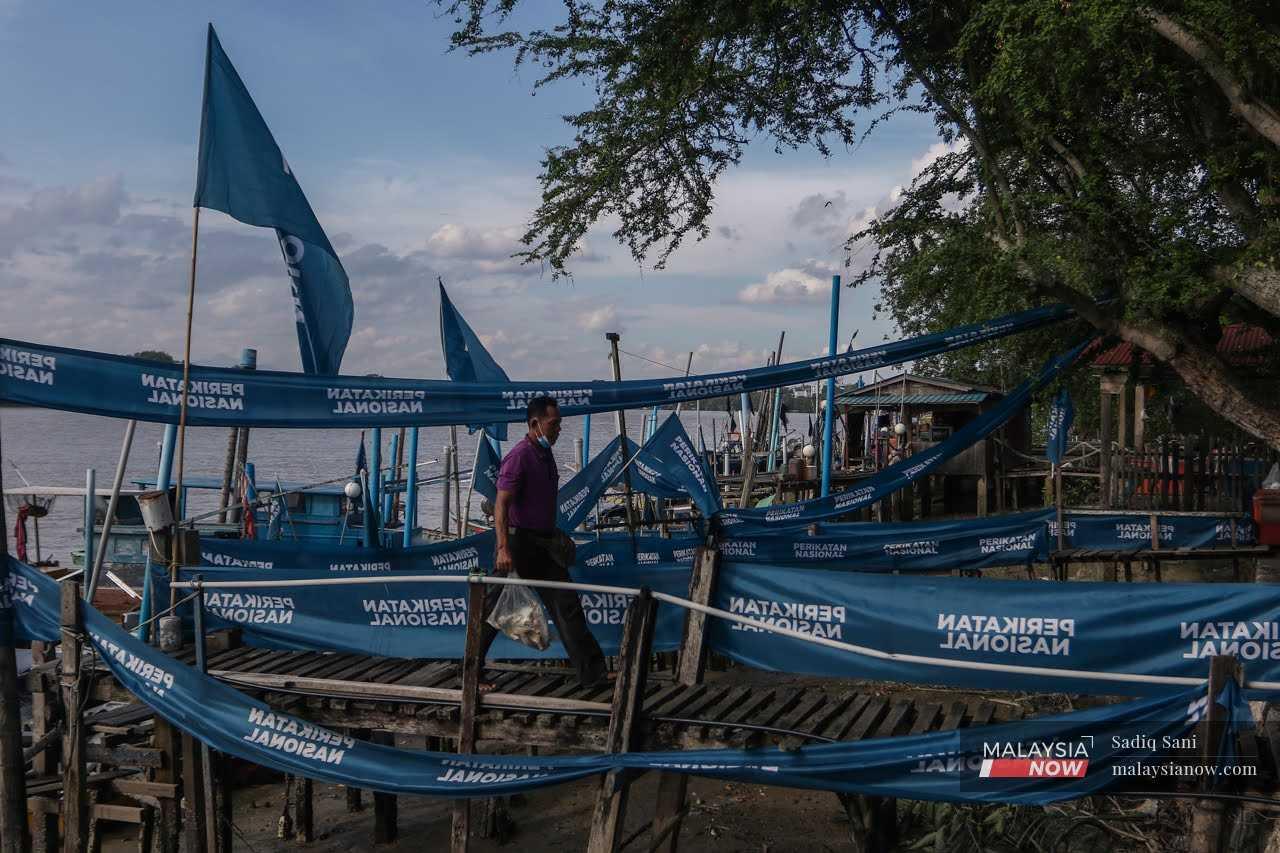 A fisherman crosses a jetty in Muar, hung about with Perikatan Nasional flags, ahead of the Johor election in March. 