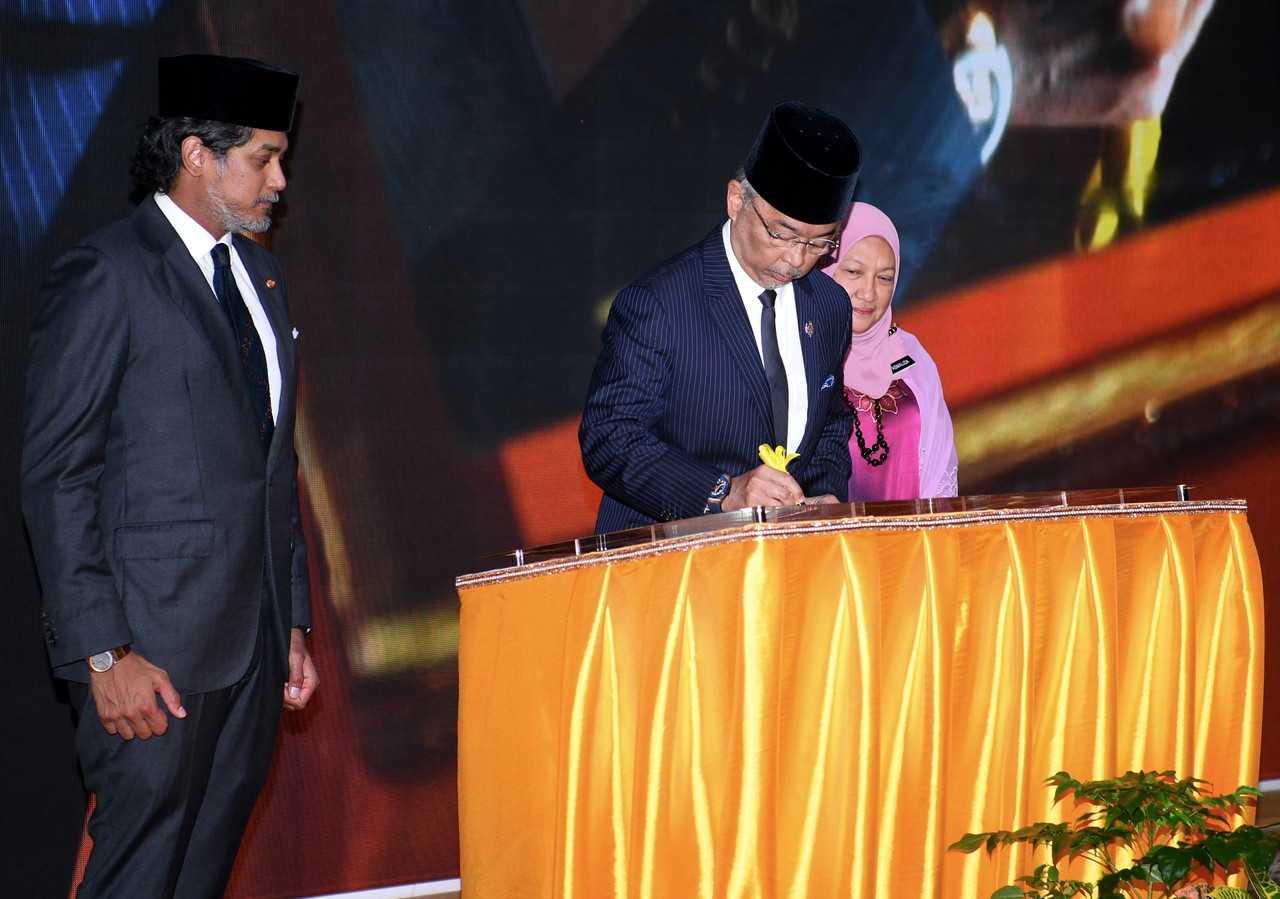 Yang di-Pertuan Agong Sultan Abdullah Sultan Ahmad Shah (tengah) menandatangani plak perasmian Institut Kesihatan Negara (NIH) di Setia Alam hari ini sambil diperhatikan Menteri Kesihatan Khairy Jamaluddin. Gambar: Bernama
