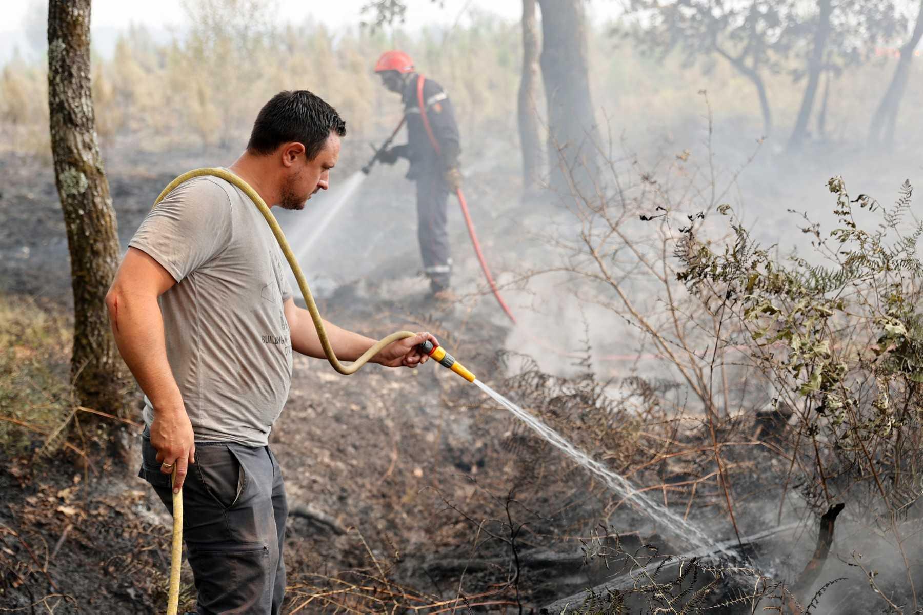 A villager helps the firemen to wet the ground so that the fire does not reignite in Louchats, western France, on July 19. Photo: AFP