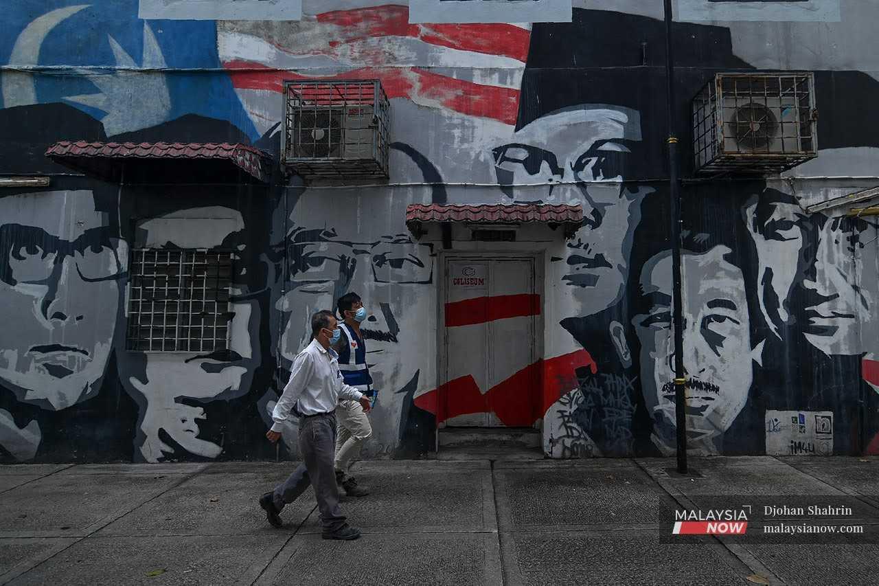 Dua lelaki berjalan di hadapan dinding yang dihiasi mural wajah bekas perdana menteri Malaysia di Jalan Coliseum, Kuala Lumpur.
