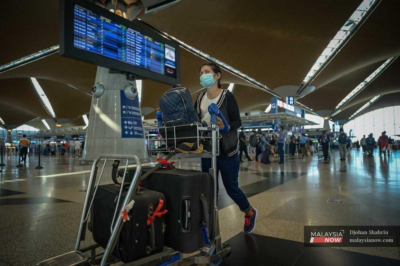 A passenger pushes her luggage trolley past a large screen showing flight departure times at KLIA in Sepang.
