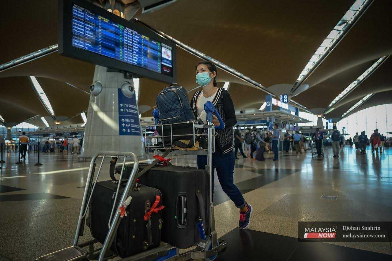 Seorang penumpang menolak troli bagasi di hadapan skrin paparan perlepasan penerbangan di KLIA, Sepang.