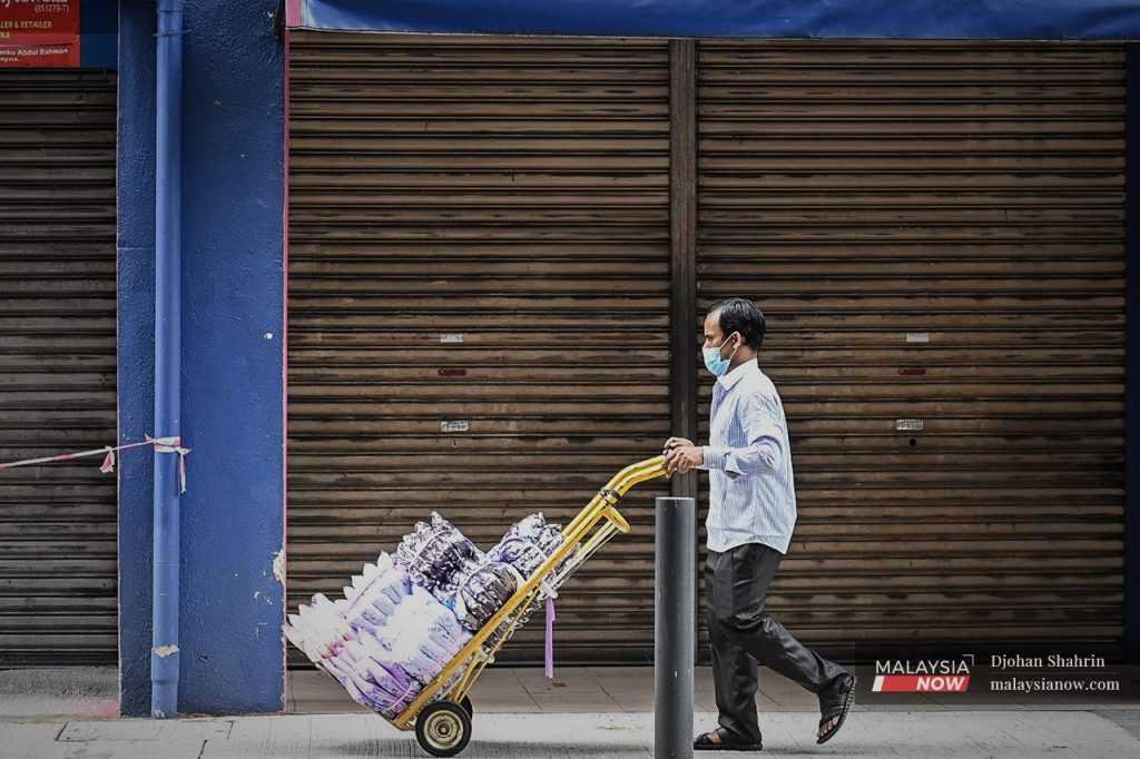 A worker pushes a trolley of textile goods past a row of closed shops in Jalan Tuanku Abdul Rahman in Kuala Lumpur.