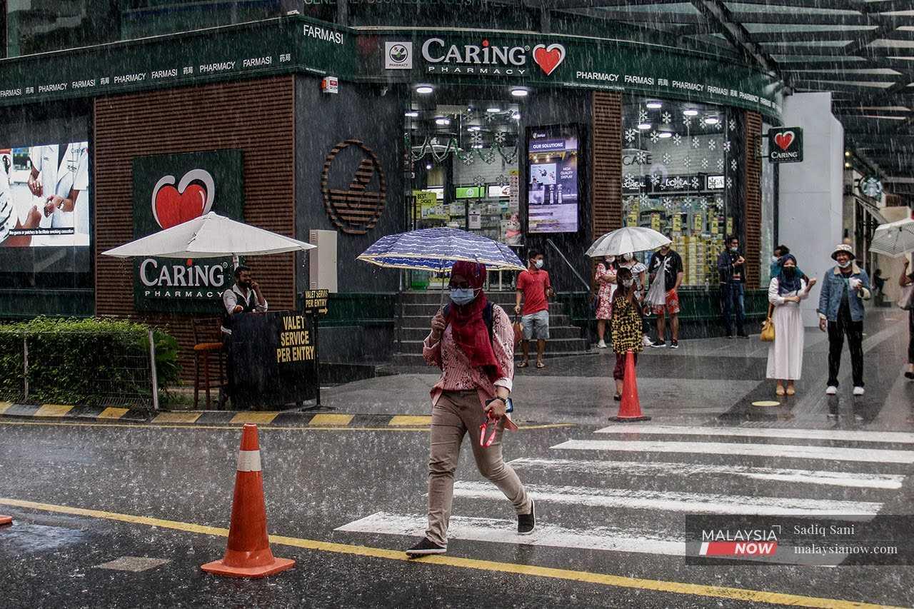 A woman holds an umbrella over her head to protect herself from the rain as she crosses a street in Bukit Bintang, Kuala Lumpur. 
