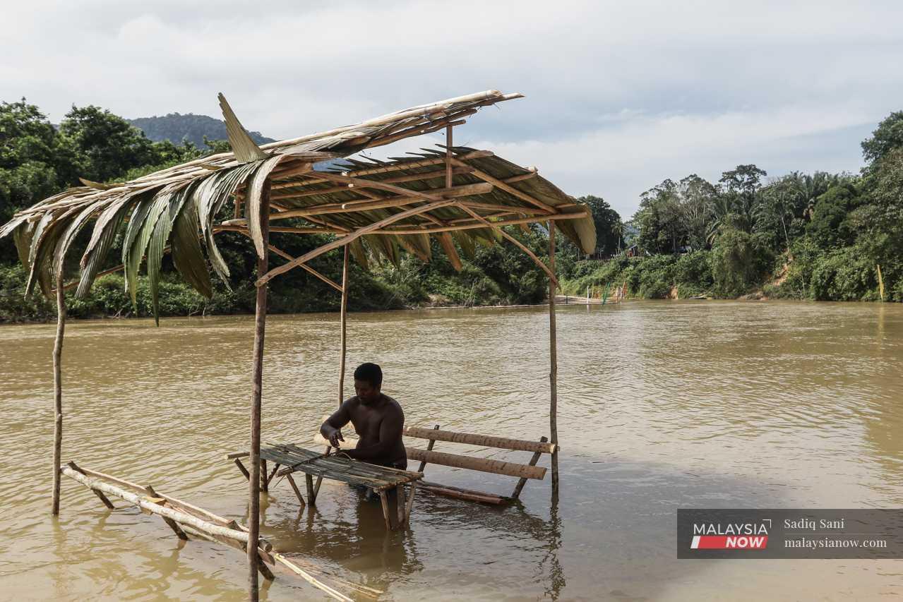 At the river, an Orang Asli man builds a makeshift hut to be used during the celebration in the shallow water near the bank. 