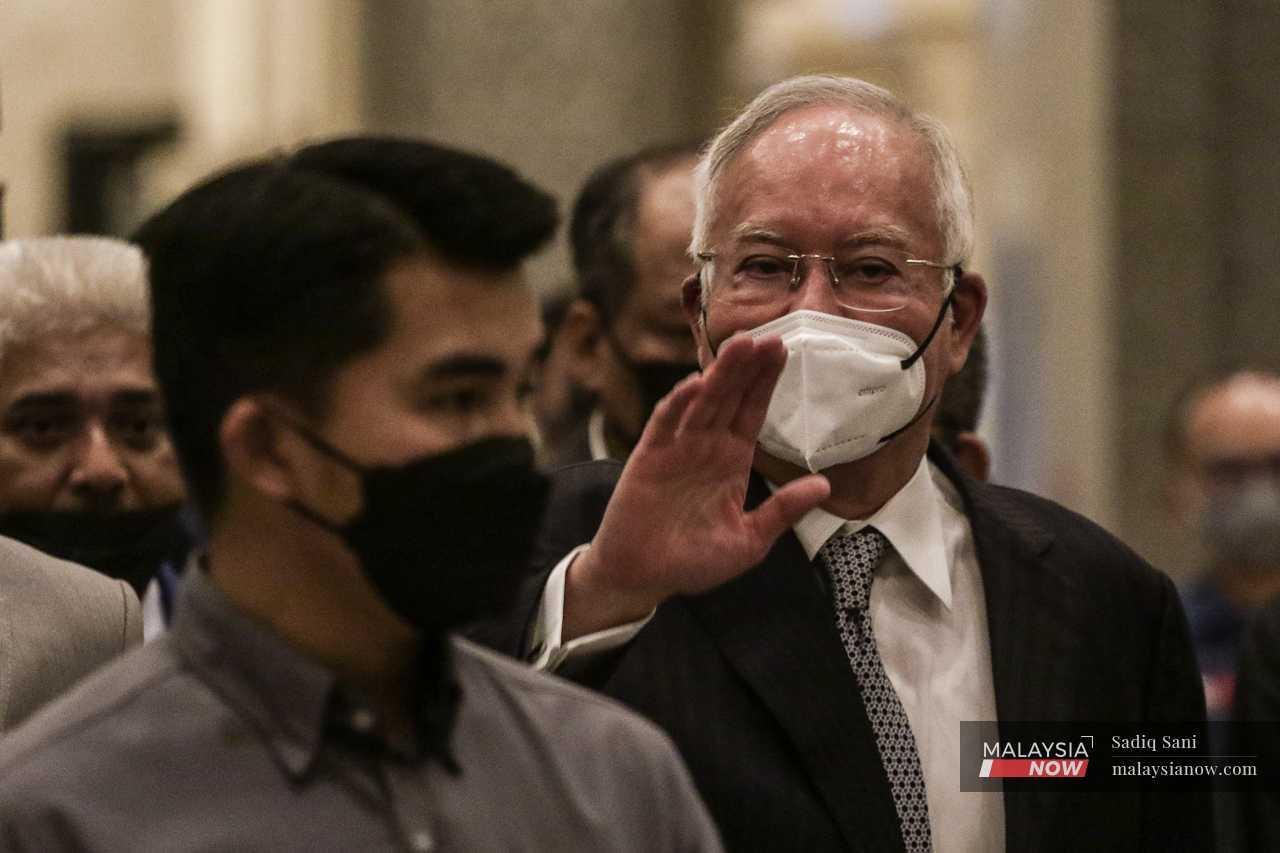 Najib waves to the media as he heads to the cafeteria during a lunch break. 
