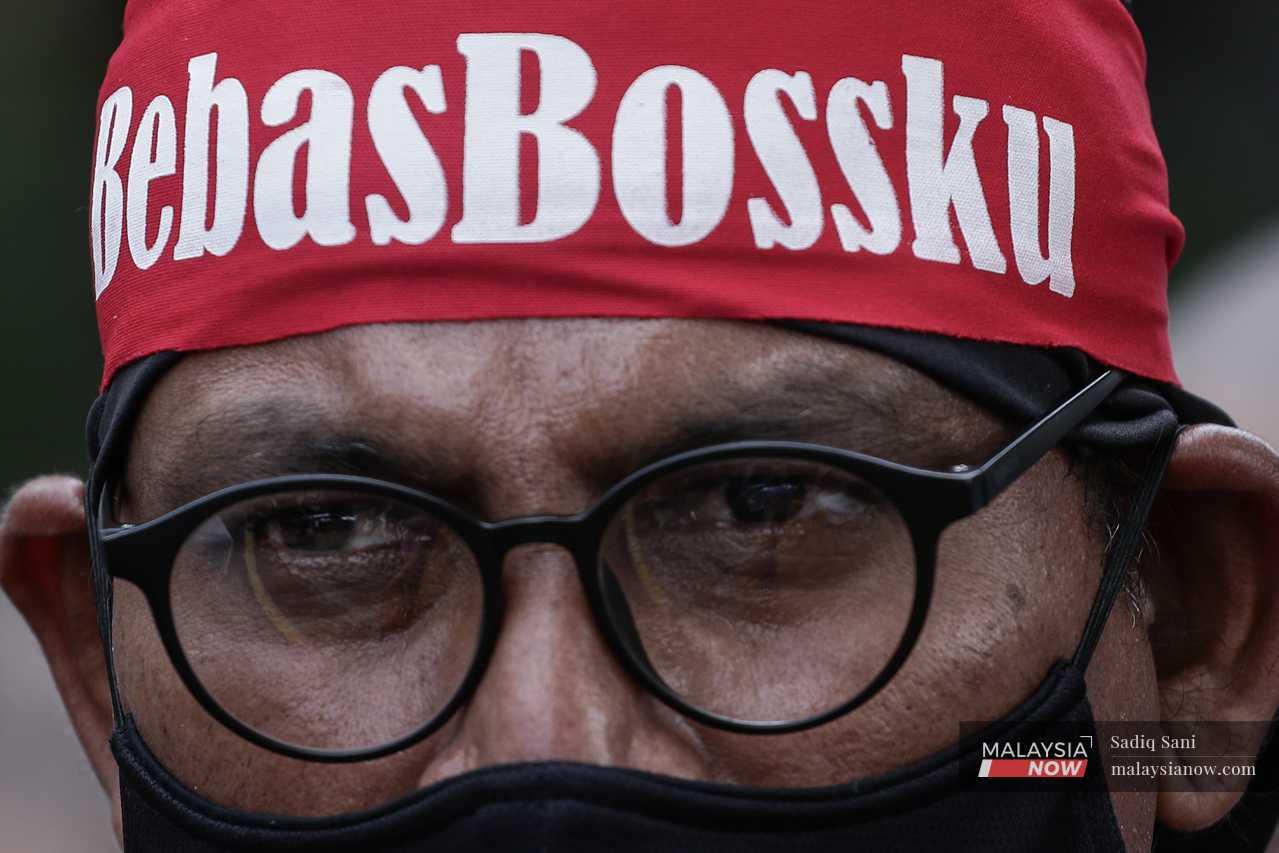 A man wears a headband reading 'Bebas Bossku' (Free Bossku), a reference to the moniker Najib assumed during his post-GE14 rebranding efforts. 