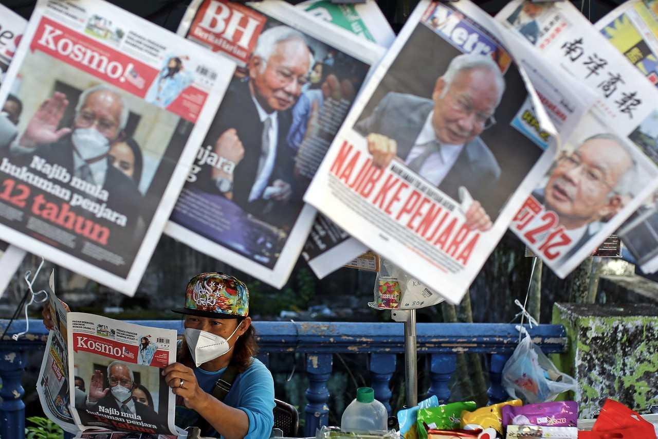 A newspaper vendor reads the day's headlines after the Federal Court's historic decision yesterday to uphold Najib Razak's SRC International conviction and sentence, sending the former prime minister to Kajang Prison to begin serving his jail term. Photo: Bernama