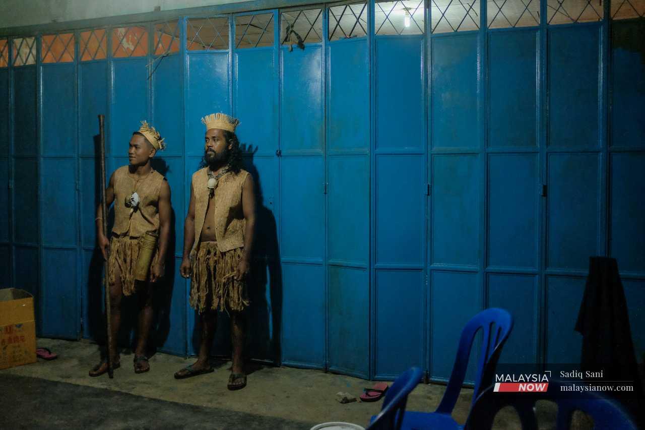 Dua orang penduduk kampung berdiri, lengkap berpakaian tradisional.