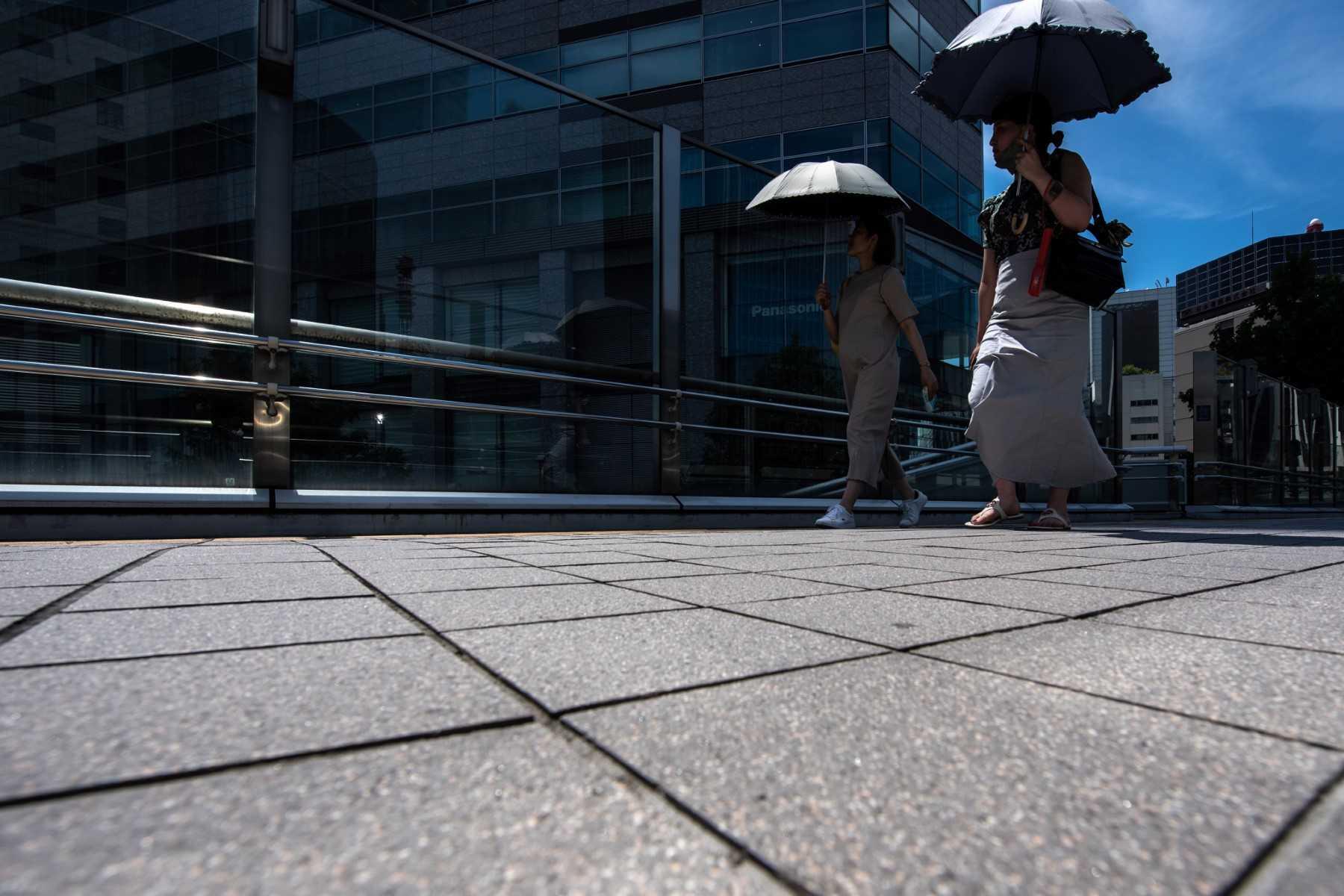Pedestrians carrying umbrellas to shade themselves from the heat walk on a footbridge in a business district Tokyo on June 29. Photo: AFP