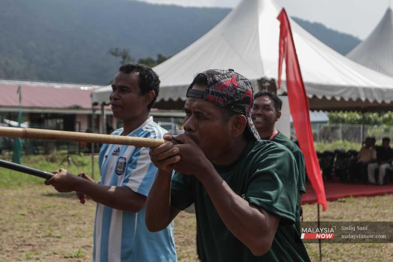 An Orang Asli man squints at the target in the distance as he prepares to blow a projectile from the pipe. 