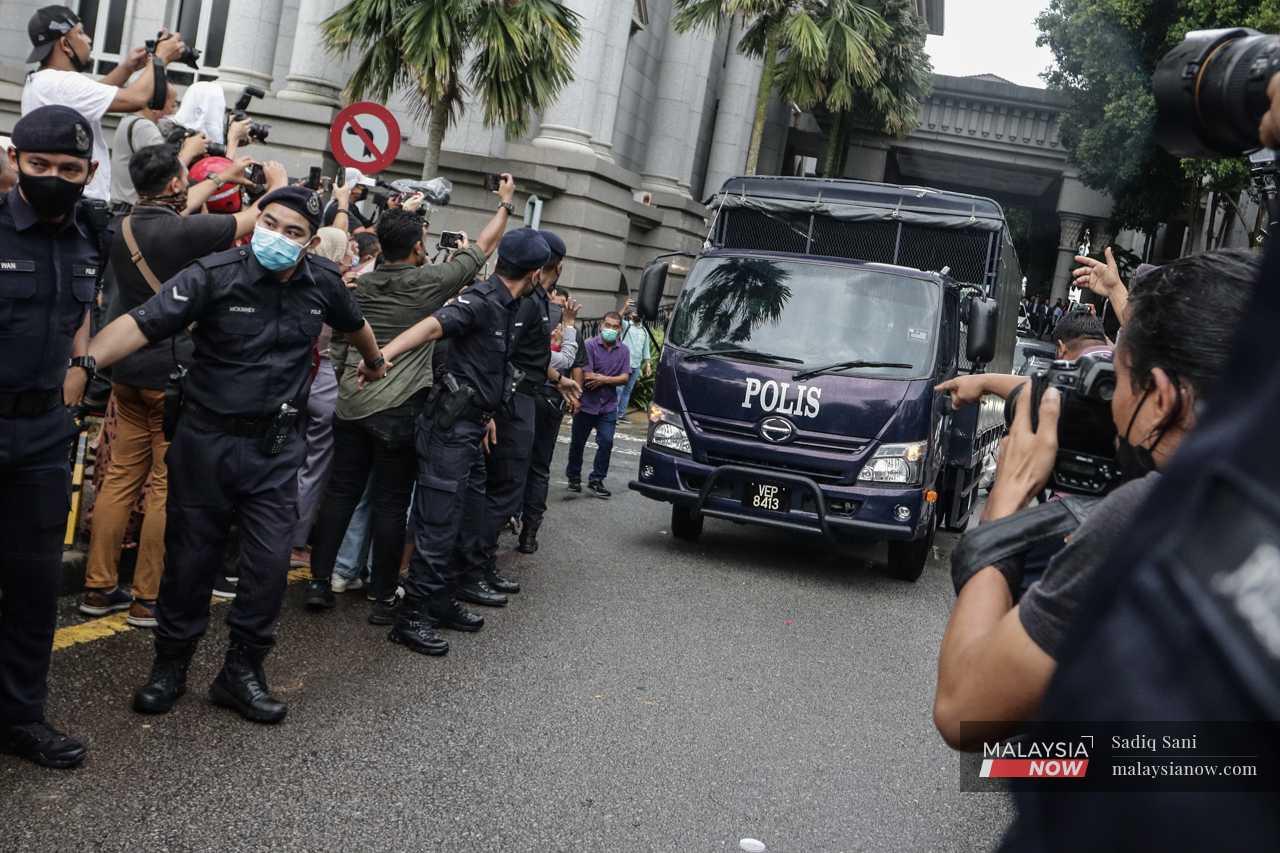 Pegawai polis berkawal memastikan  orang ramai tidak merempuh ketika trak polis keluar dari perkarangan mahkamah.
