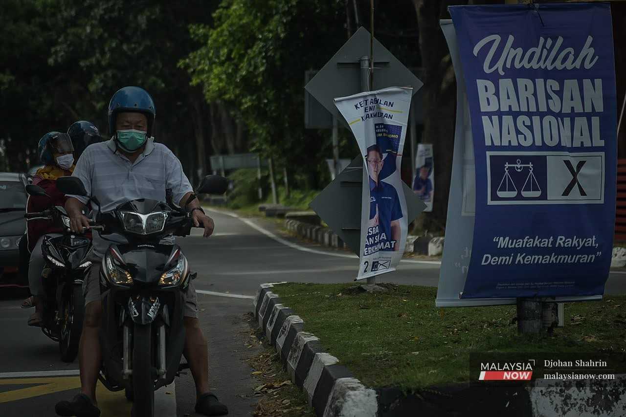 Motorcyclists wait at a red light at a junction hung about with Barisan Nasional posters ahead of the Melaka state election in November last year.