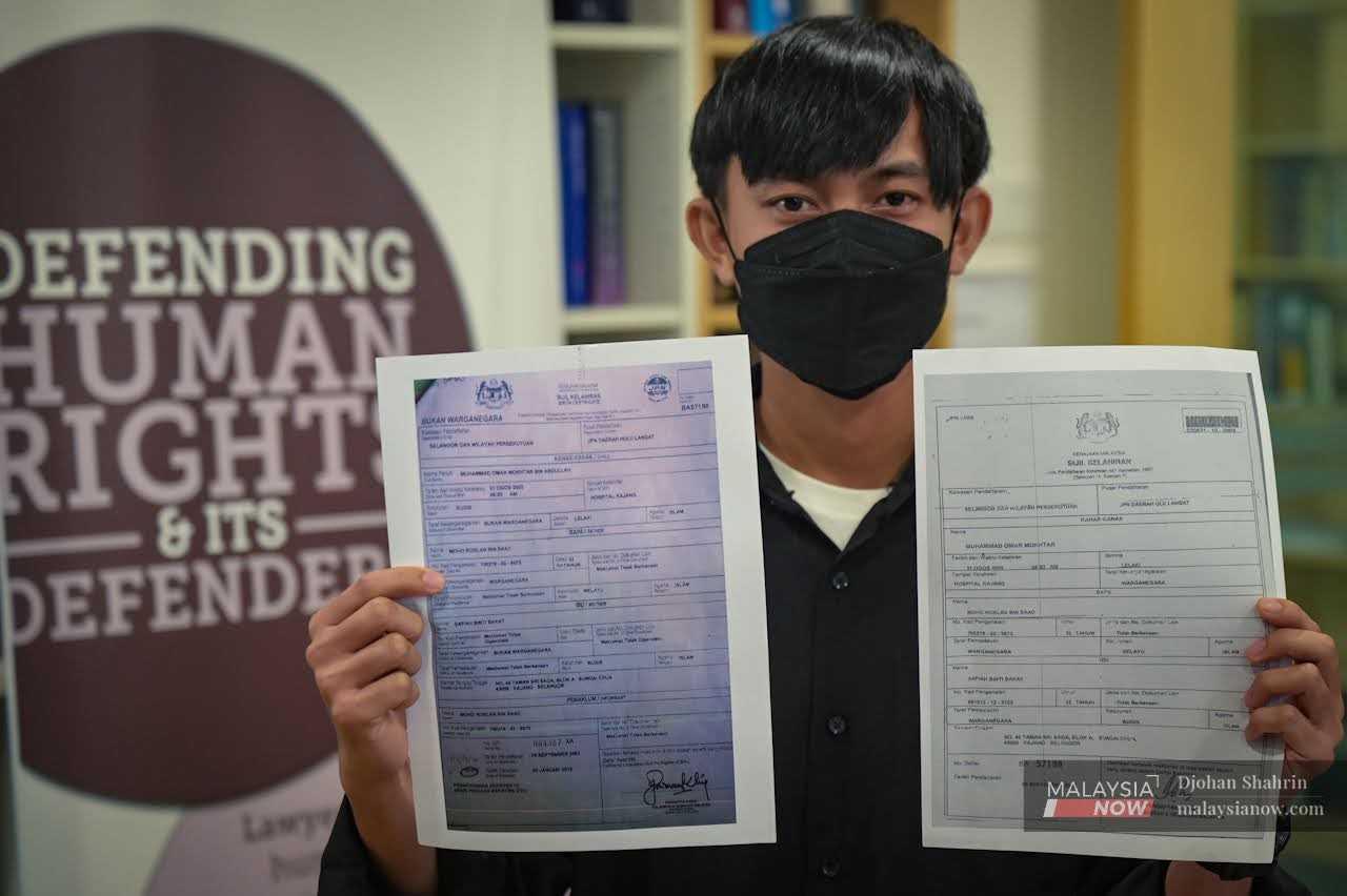Mohamad Omar Mokhtar holds up a copy of his birth certificate (right) and the document denying him citizenship at a press conference in Petaling Jaya. 
